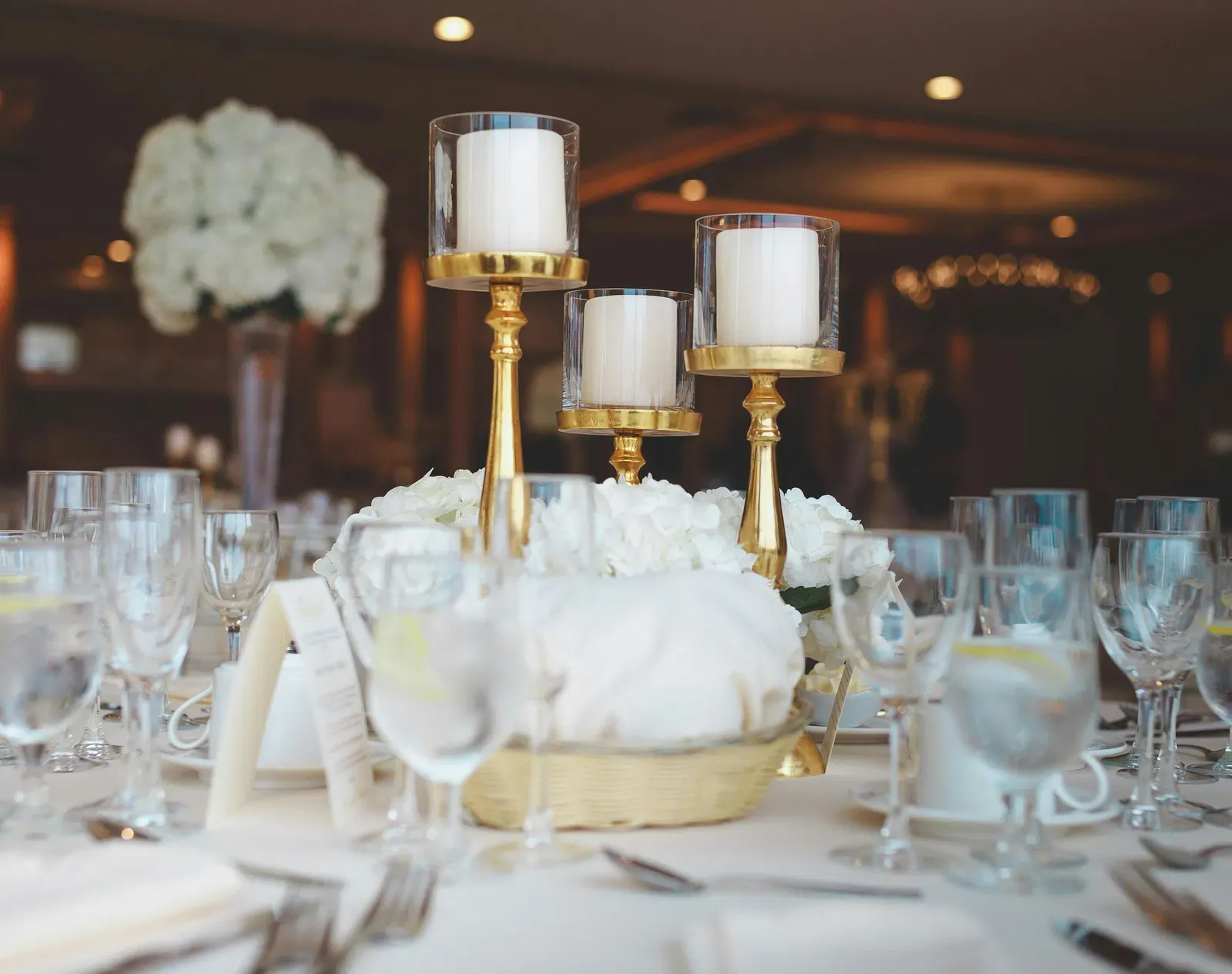 Selective focus photography of a centre table decorated with candles and wine glasses on a white cloth.