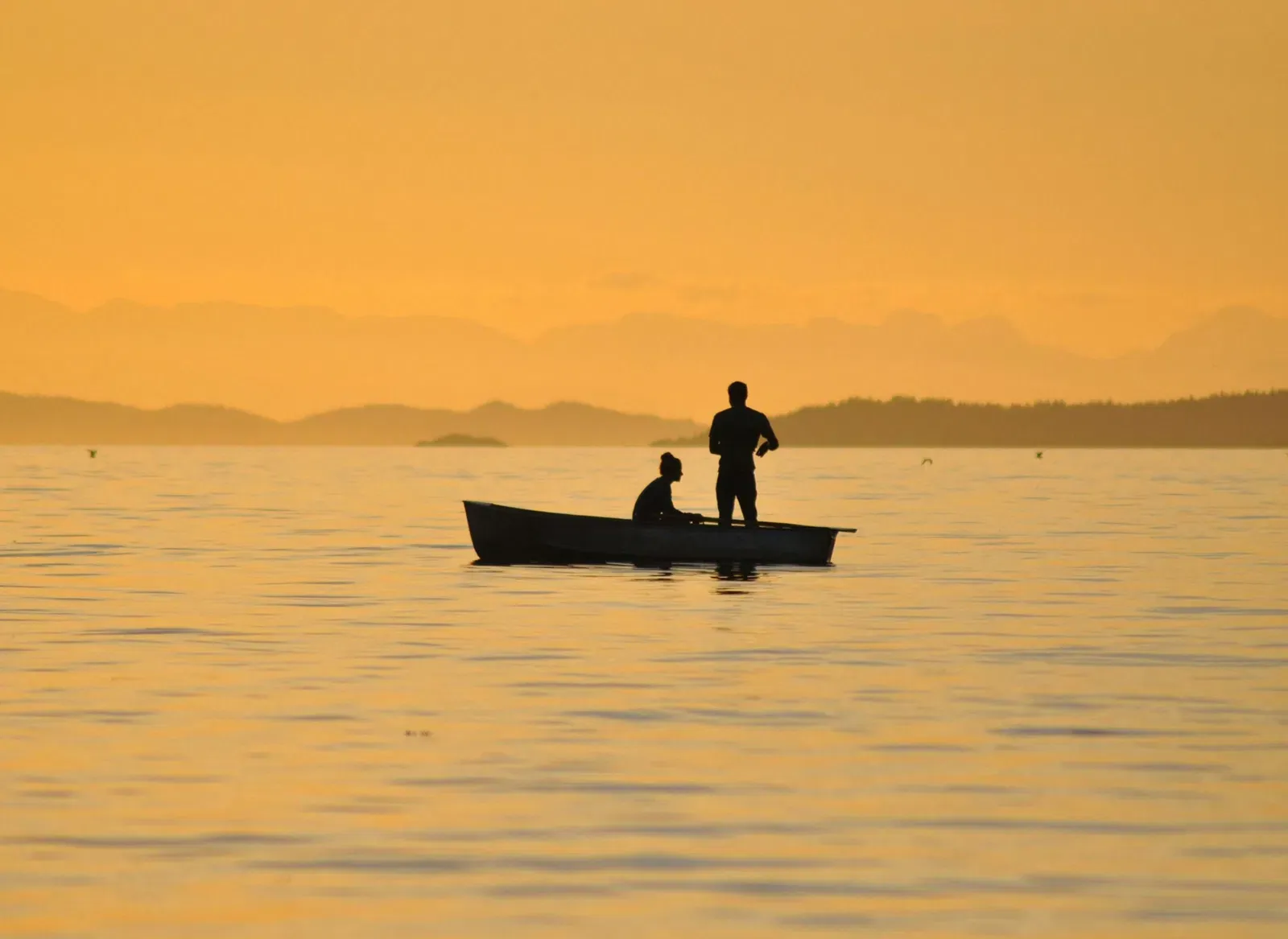 Two people on a boat in a body of water at sunset.