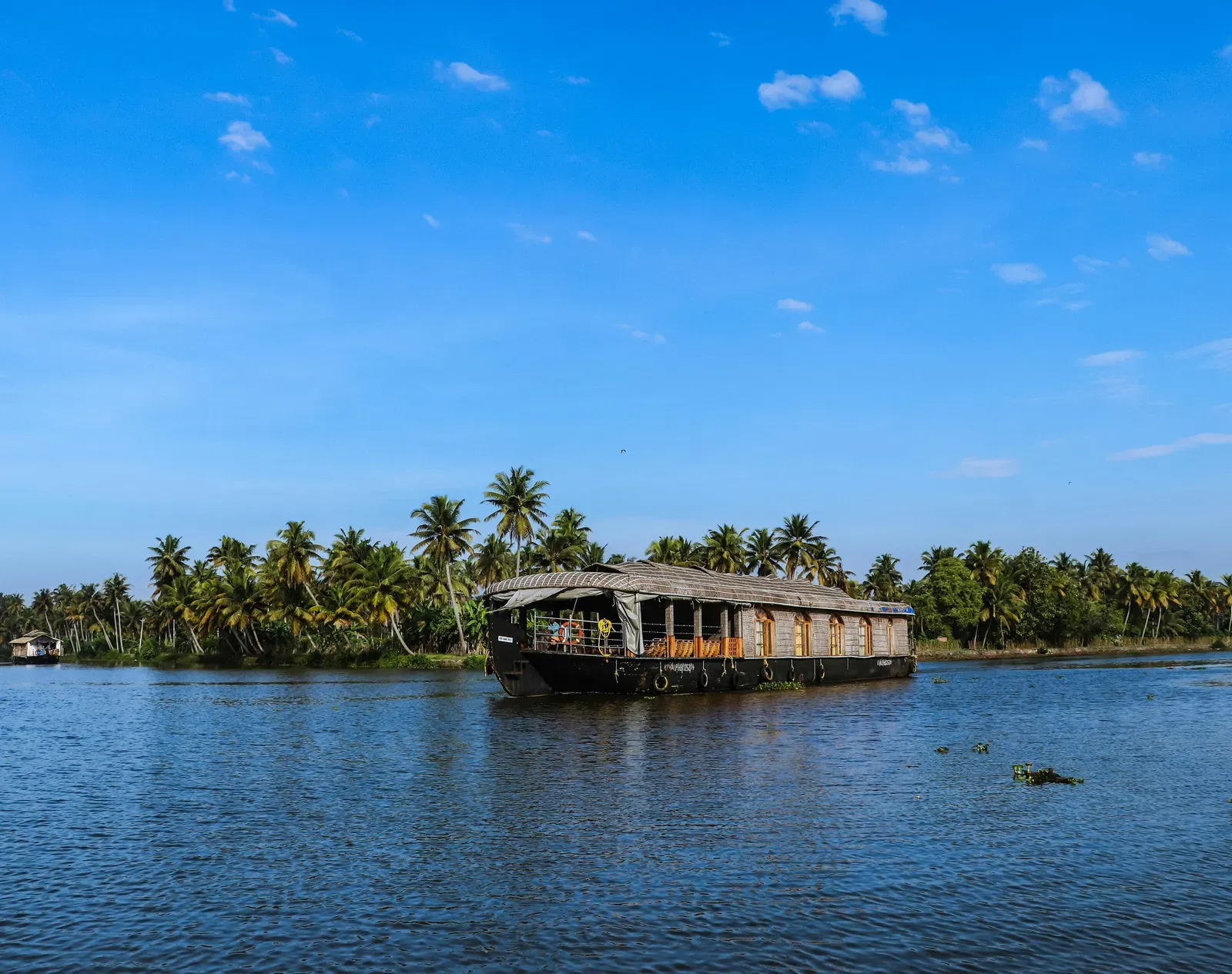 A houseboat sailing in water with palm trees in the background in Kerala.